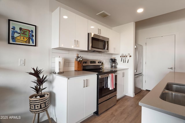 kitchen with tasteful backsplash, white cabinetry, sink, stainless steel appliances, and light hardwood / wood-style flooring