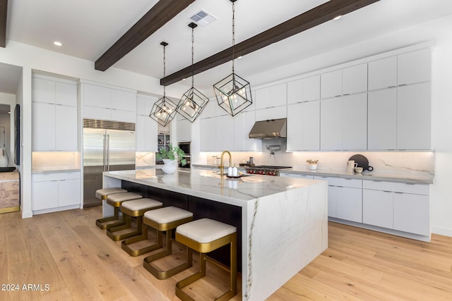 kitchen with decorative light fixtures, stainless steel built in refrigerator, sink, white cabinets, and a large island with sink