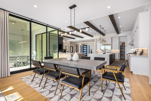 dining room with sink, light wood-type flooring, expansive windows, ceiling fan, and beam ceiling