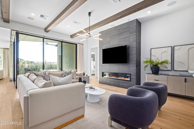 living room featuring beamed ceiling, a tile fireplace, an inviting chandelier, and light wood-type flooring