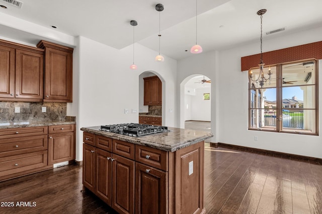 kitchen with stainless steel gas cooktop, light stone countertops, pendant lighting, a kitchen island, and decorative backsplash