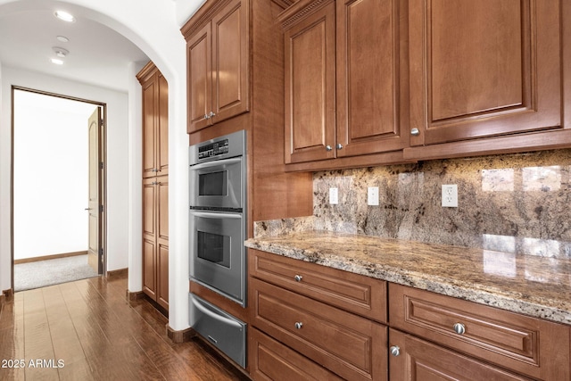 kitchen with light stone counters, dark hardwood / wood-style flooring, stainless steel double oven, and tasteful backsplash