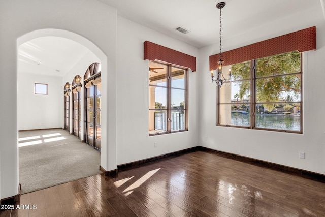 unfurnished room with dark hardwood / wood-style floors, a chandelier, and a water view