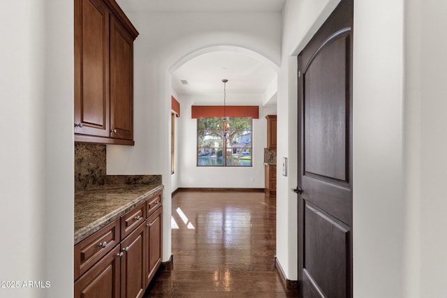 interior space with decorative light fixtures, stone counters, dark wood-type flooring, and tasteful backsplash