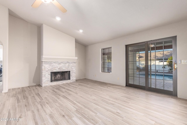 unfurnished living room with ceiling fan, a stone fireplace, light wood-type flooring, and vaulted ceiling