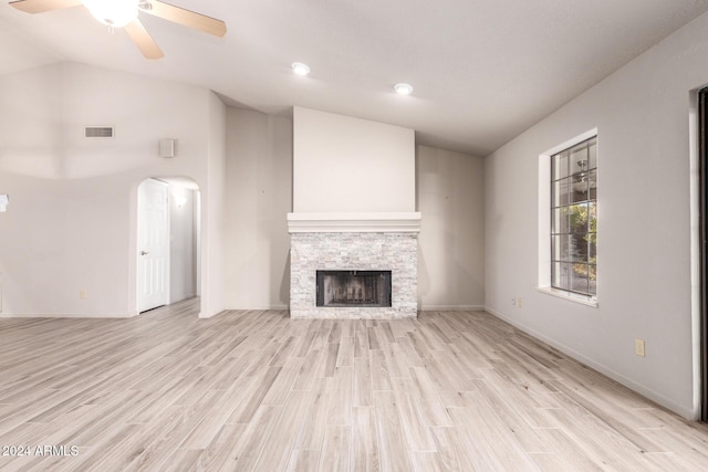 unfurnished living room with ceiling fan, a stone fireplace, lofted ceiling, and light wood-type flooring