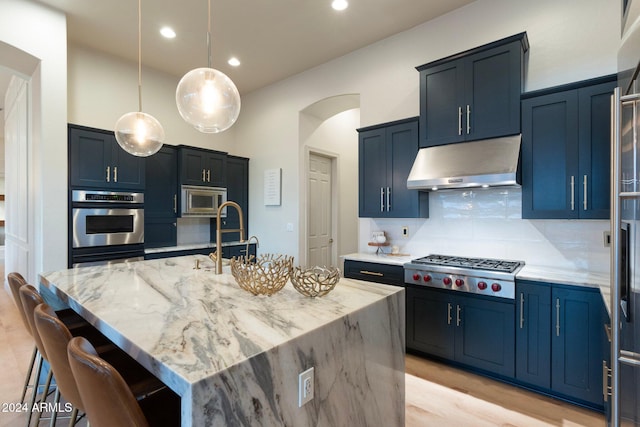 kitchen with a center island with sink, decorative backsplash, light stone counters, and stainless steel appliances