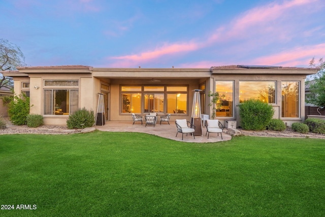 back house at dusk with solar panels, a patio area, and a yard