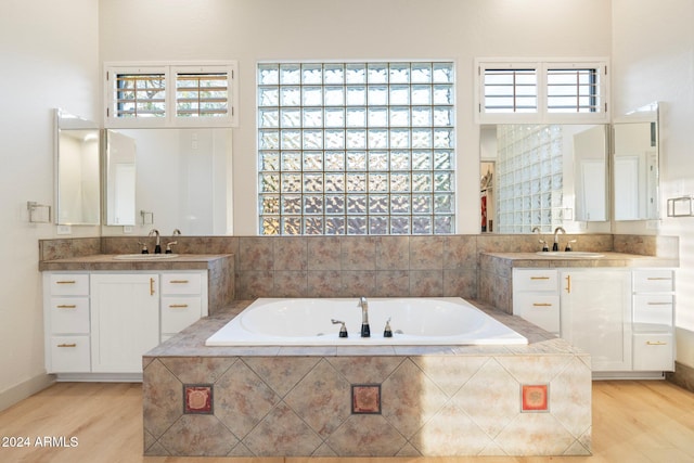 bathroom featuring wood-type flooring, vanity, and a relaxing tiled tub