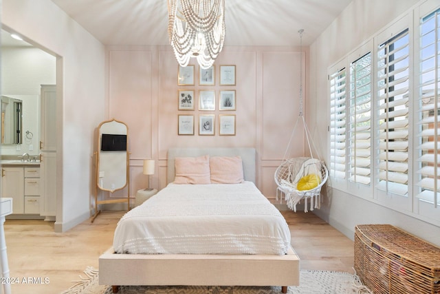 bedroom featuring connected bathroom, sink, light hardwood / wood-style flooring, and an inviting chandelier