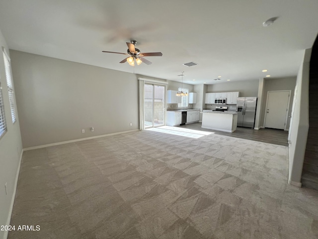 unfurnished living room with light colored carpet and ceiling fan with notable chandelier