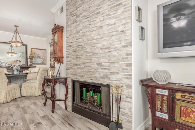 living area with crown molding, a stone fireplace, and light hardwood / wood-style floors