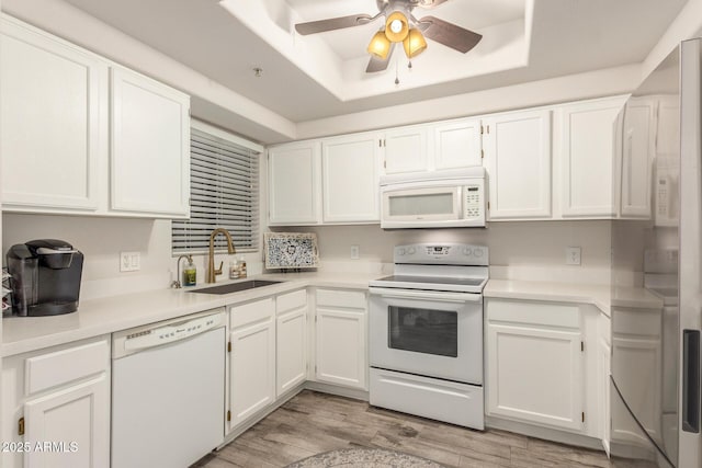 kitchen featuring white cabinetry, sink, white appliances, a tray ceiling, and light wood-type flooring