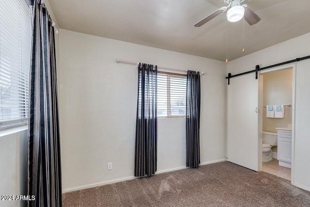 unfurnished bedroom with carpet floors, a barn door, ensuite bathroom, and ceiling fan