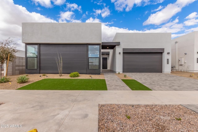 view of front of house featuring decorative driveway, an attached garage, and stucco siding