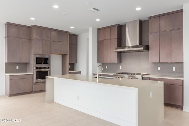 kitchen featuring light countertops, backsplash, appliances with stainless steel finishes, a sink, and wall chimney exhaust hood