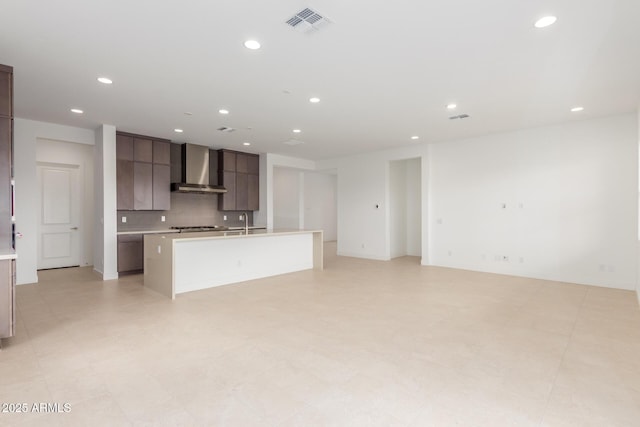 kitchen with light countertops, visible vents, backsplash, a kitchen island with sink, and wall chimney exhaust hood