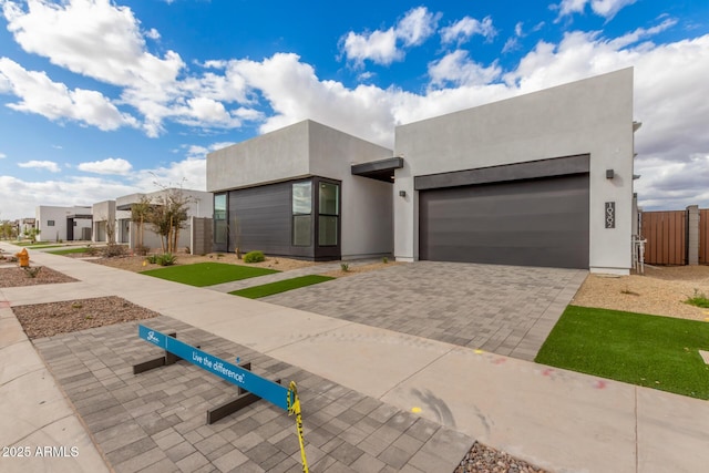 view of front facade featuring decorative driveway, stucco siding, an attached garage, a gate, and fence