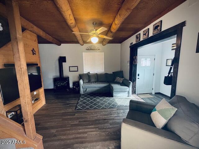 living room with ceiling fan, wooden ceiling, beamed ceiling, dark hardwood / wood-style floors, and a wood stove