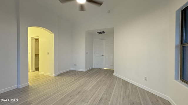 spare room featuring arched walkways, visible vents, light wood-style flooring, ceiling fan, and baseboards