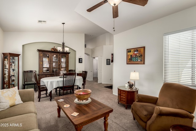 carpeted living room with a ceiling fan, visible vents, arched walkways, vaulted ceiling, and baseboards