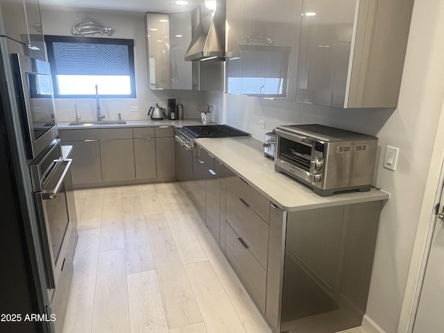 kitchen featuring light wood finished floors, wall chimney range hood, gray cabinets, a sink, and modern cabinets