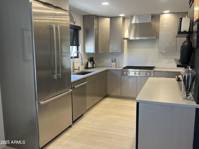 kitchen with light wood finished floors, wall chimney range hood, a sink, gray cabinetry, and appliances with stainless steel finishes