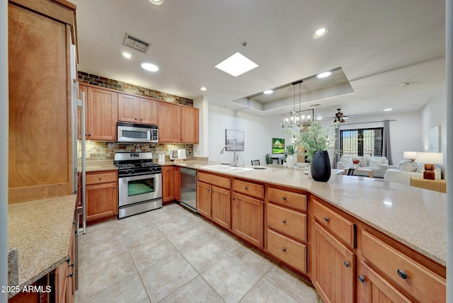 kitchen featuring stainless steel appliances, tasteful backsplash, a raised ceiling, a sink, and a peninsula