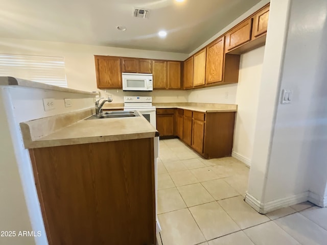 kitchen featuring brown cabinetry, light tile patterned flooring, white appliances, baseboards, and a sink