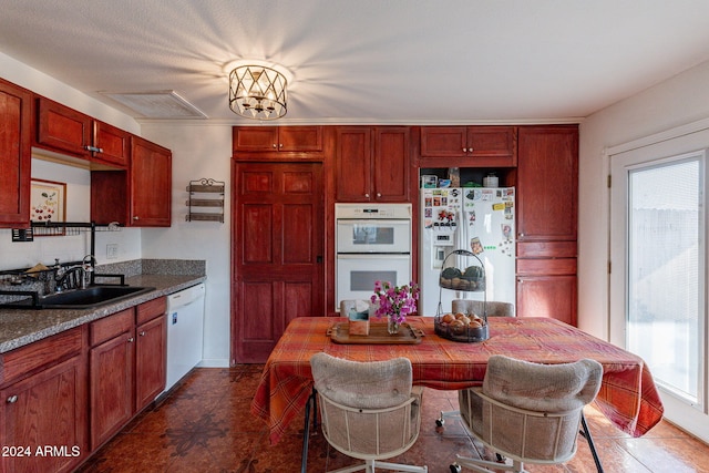 kitchen featuring an inviting chandelier, sink, white appliances, and dark stone countertops