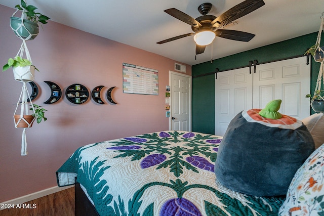 bedroom with hardwood / wood-style floors, a barn door, a closet, and ceiling fan