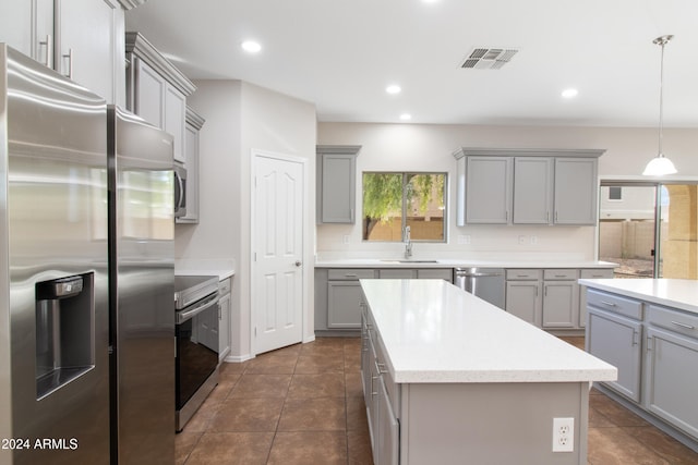 kitchen with dark tile patterned floors, gray cabinetry, stainless steel appliances, a center island, and decorative light fixtures