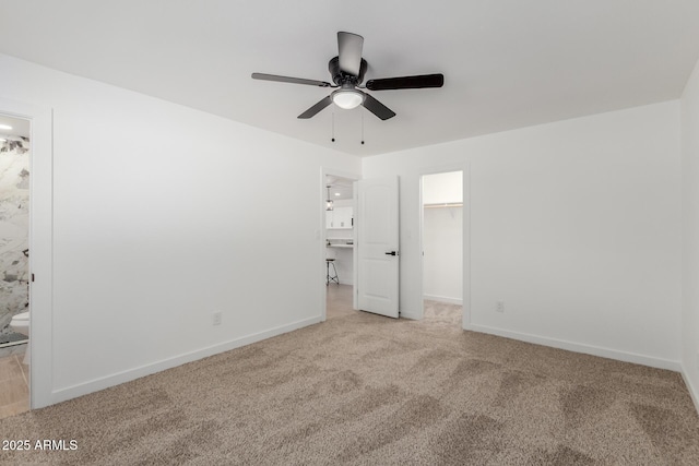 unfurnished bedroom featuring baseboards, a ceiling fan, ensuite bath, a spacious closet, and carpet flooring