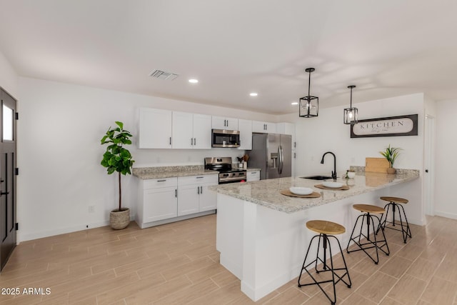 kitchen with visible vents, appliances with stainless steel finishes, a peninsula, a kitchen bar, and a sink