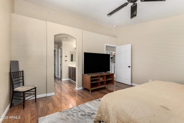 bedroom featuring arched walkways, baseboards, wood finished floors, and ensuite bathroom