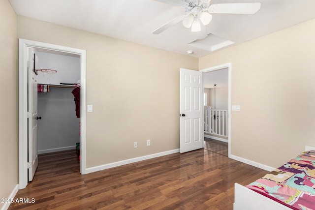 unfurnished bedroom with ceiling fan, a walk in closet, baseboards, and wood finished floors