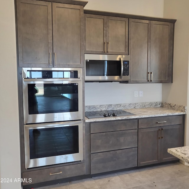 kitchen with light stone counters, dark brown cabinets, stainless steel appliances, and light tile patterned flooring