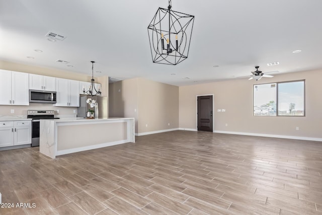 kitchen featuring appliances with stainless steel finishes, ceiling fan with notable chandelier, a kitchen island, white cabinetry, and hanging light fixtures