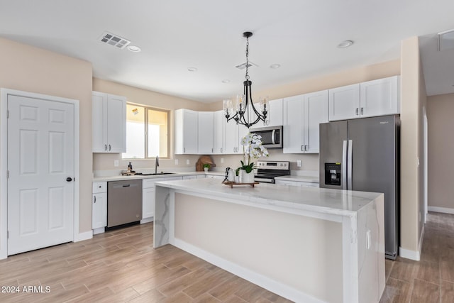 kitchen featuring a center island, an inviting chandelier, pendant lighting, white cabinets, and appliances with stainless steel finishes