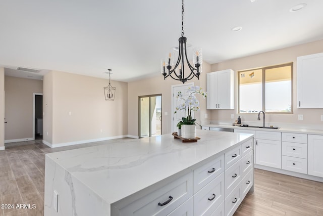 kitchen featuring light stone countertops, sink, a kitchen island, pendant lighting, and white cabinets