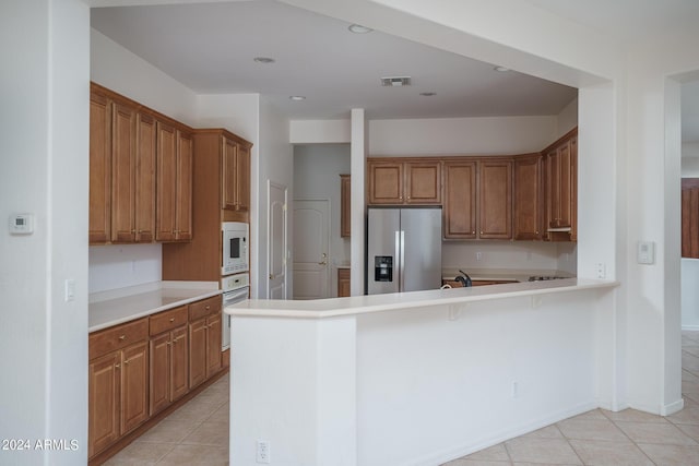 kitchen with a kitchen bar, light tile patterned floors, white appliances, and kitchen peninsula