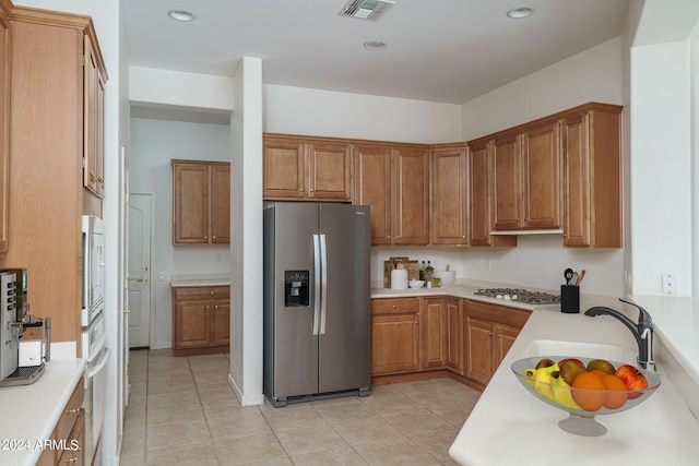 kitchen with stainless steel refrigerator with ice dispenser, sink, gas stovetop, light tile patterned floors, and wall oven