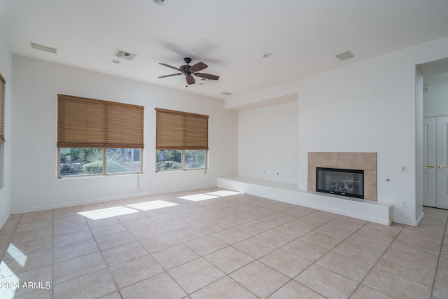 unfurnished living room featuring a tiled fireplace, light tile patterned floors, and ceiling fan