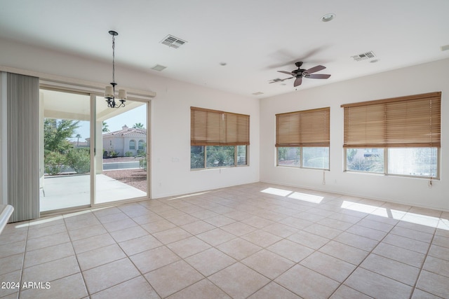 spare room with light tile patterned floors, ceiling fan with notable chandelier, and a wealth of natural light