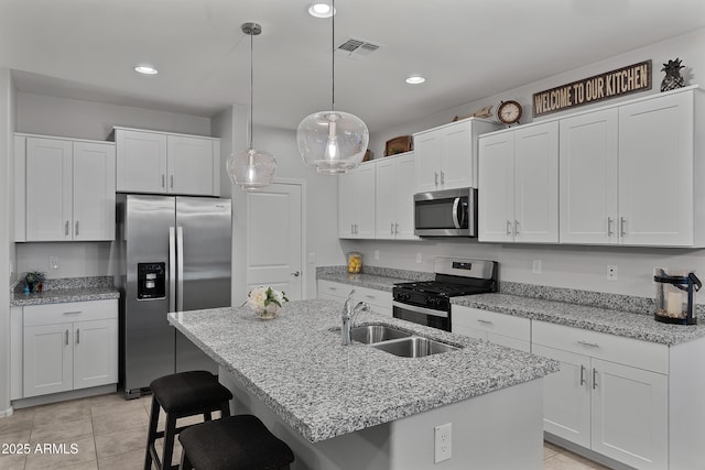 kitchen featuring a kitchen island with sink, stainless steel appliances, white cabinetry, pendant lighting, and a sink