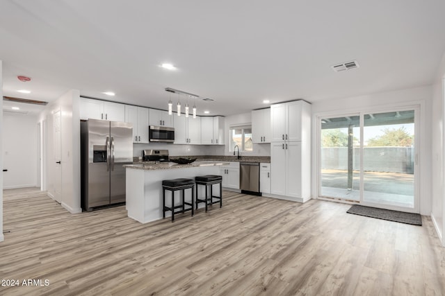 kitchen featuring decorative light fixtures, white cabinetry, a kitchen bar, a center island, and stainless steel appliances