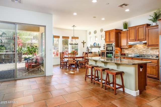 kitchen featuring a breakfast bar, sink, decorative light fixtures, a center island with sink, and black electric stovetop