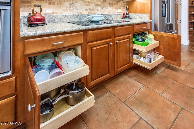 kitchen featuring high end fridge, decorative backsplash, light stone countertops, and black electric cooktop