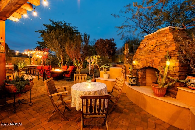 patio terrace at dusk featuring an outdoor stone fireplace and an outdoor fire pit