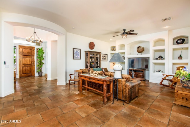 living room featuring ceiling fan with notable chandelier and built in features